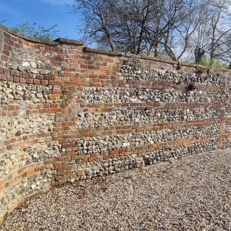 Flint and brick boundary wall being repaired and repointed in lime mortar