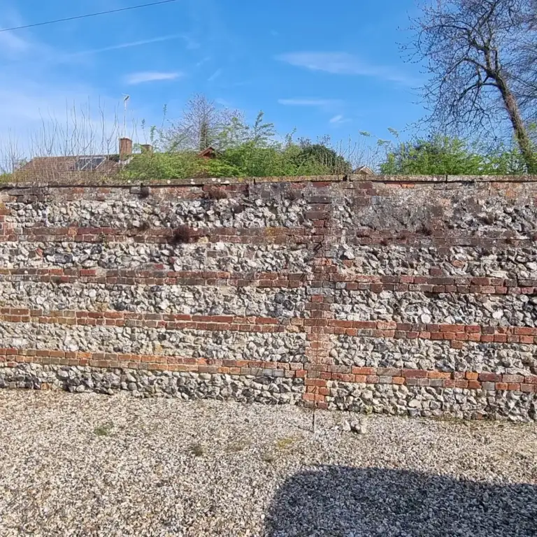 Flint and brick boundary wall being repaired and repointed in lime mortar