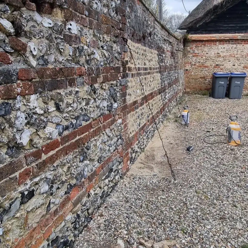 Flint and brick boundary wall being repaired and repointed in lime mortar